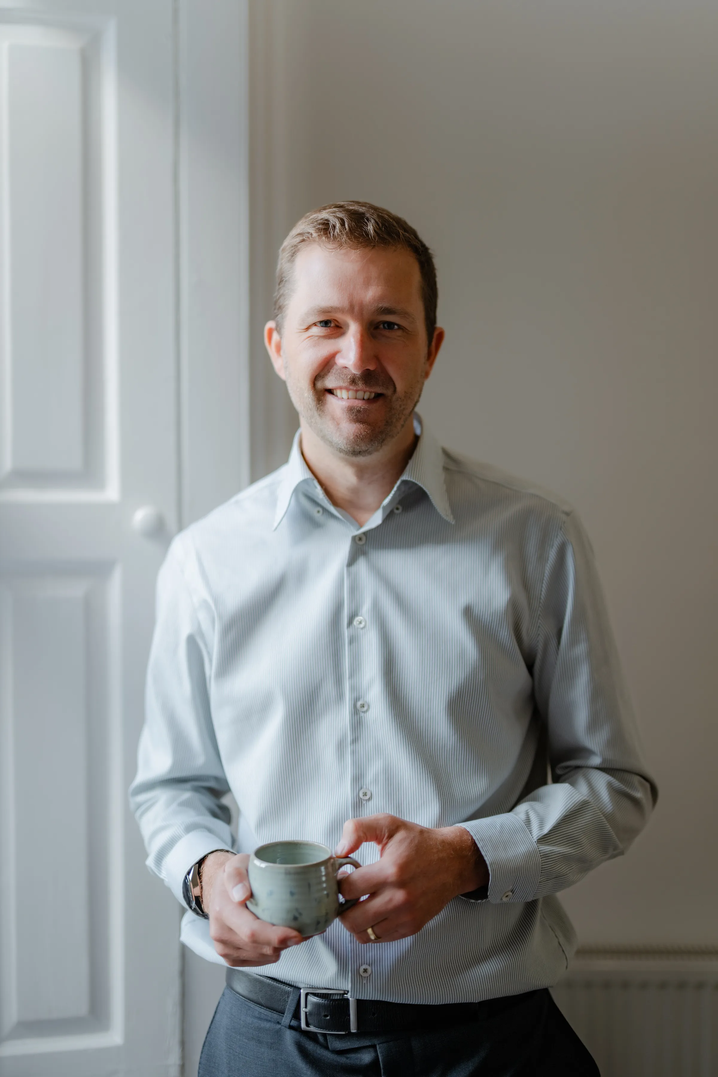 Nat Baldwin standing in a bright room holding a mug, smiling